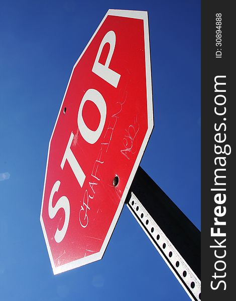 Stop sign with graffiti on it, against a clear blue sky.
