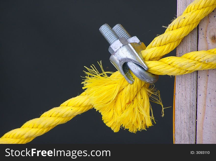 A yellow rope for a tie-down is clamped by metallic fastening. A yellow rope for a tie-down is clamped by metallic fastening