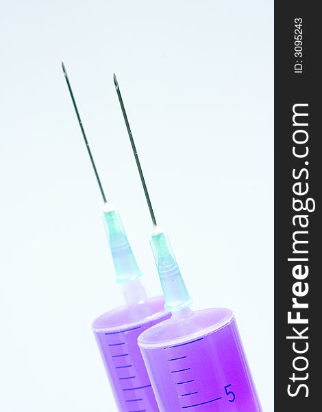 Two disposable syringes filled with purple fluid with needles against the white background. Two disposable syringes filled with purple fluid with needles against the white background