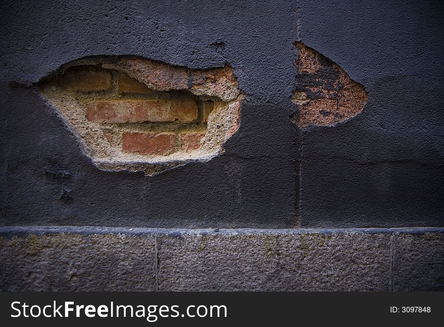 An old, broken wall in Madrid. The initial layer of brick is visible through the cracks.