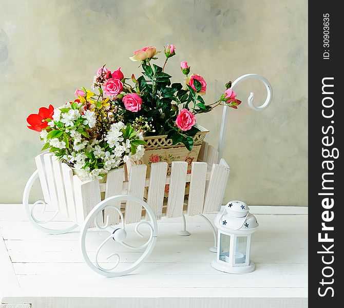 Decorative wheelbarrow with bright flowers in it and white lantern. Decorative wheelbarrow with bright flowers in it and white lantern