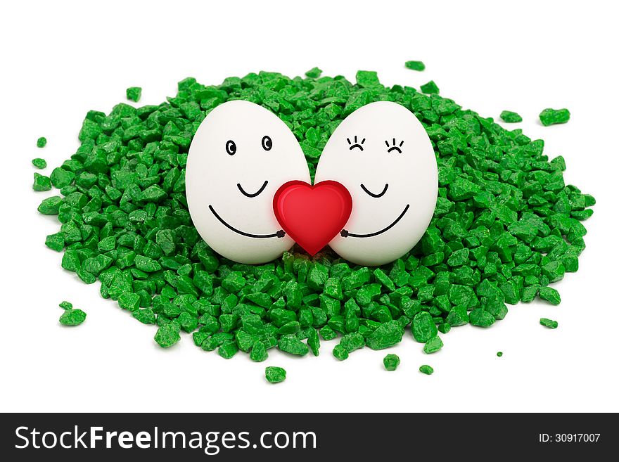 Two eggs lie on a green stones, are smiling and holding a red heart. Two eggs lie on a green stones, are smiling and holding a red heart.