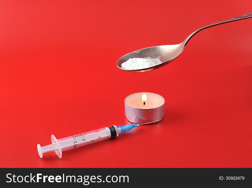 Syringe, a burning candle and a spoon with a drug against a red background. Syringe, a burning candle and a spoon with a drug against a red background