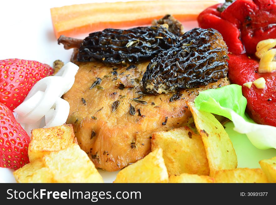 Macro shot of pork steak with Morel mushrooms, French recipe, on white plate with French fries, red pepper in olive oil with garlic, vegetables and strawberries. Macro shot of pork steak with Morel mushrooms, French recipe, on white plate with French fries, red pepper in olive oil with garlic, vegetables and strawberries