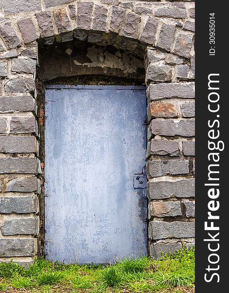 Stone wall with an arch and blue metal door, and the grass in front of it. Stone wall with an arch and blue metal door, and the grass in front of it