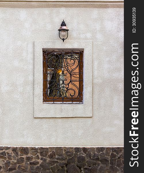 Window with wrought protection and a lantern on the wall with a stone basement. Window with wrought protection and a lantern on the wall with a stone basement