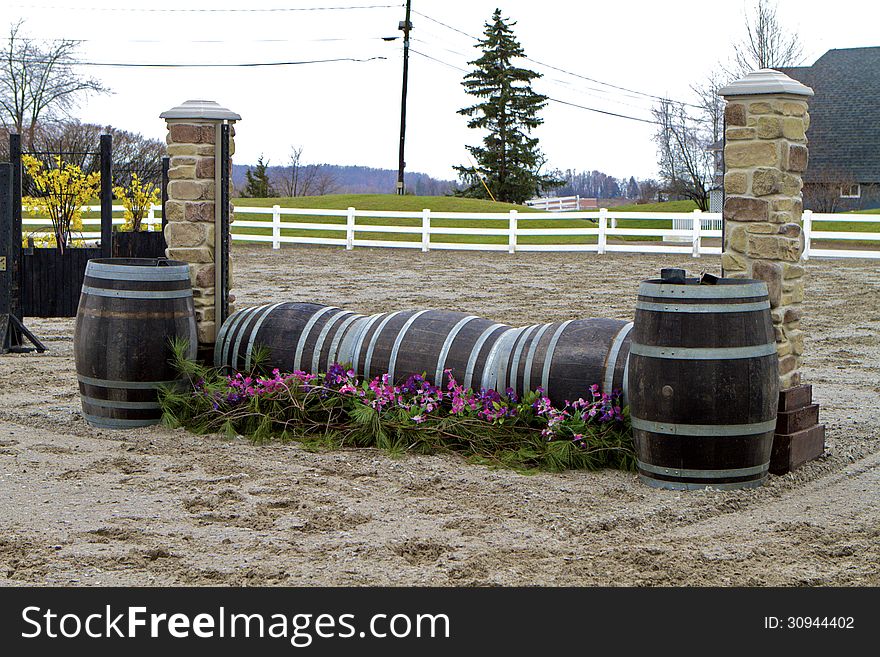 Horse jump consisting of two stone pillars and lengthwise barrels decorated with greenery and pink flowers. Horse jump consisting of two stone pillars and lengthwise barrels decorated with greenery and pink flowers.