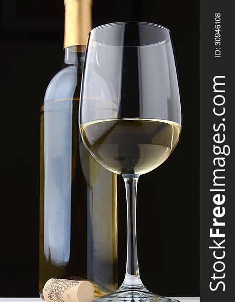 A glass of white wine with wine bottle and cork on a black background. A glass of white wine with wine bottle and cork on a black background.
