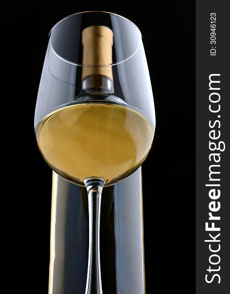 A glass of white wine and wine bottle on black.