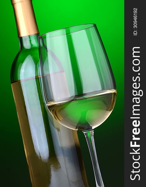 A glass of white wine and wine bottle on a green background. A glass of white wine and wine bottle on a green background