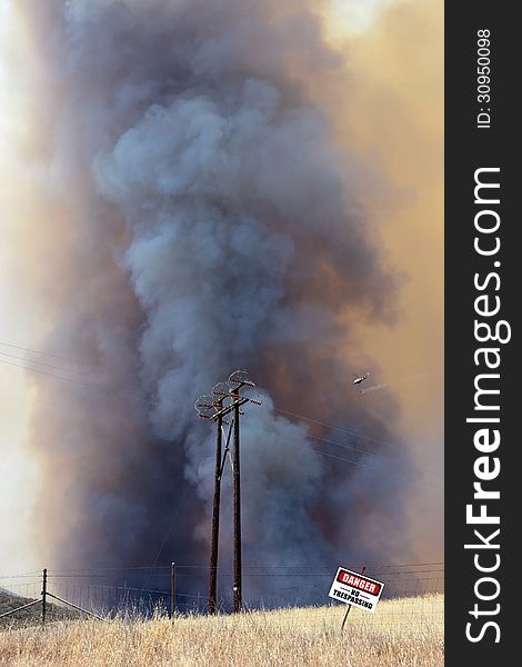 Out of control brush fire with water dropping helicopter and danger sign.