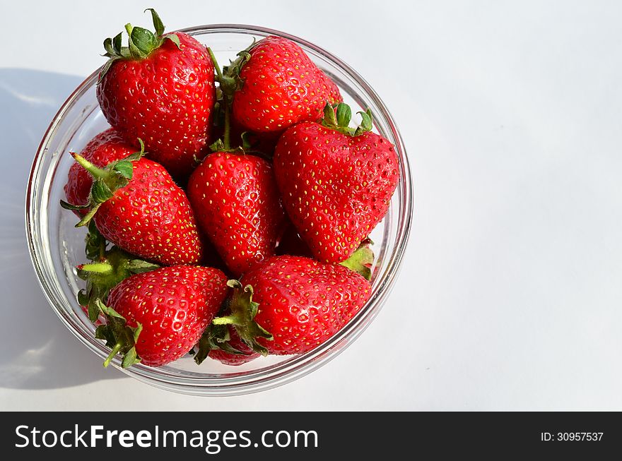 Strawberries in glass bowl in sunlight, with shadow, over white background. Strawberries in glass bowl in sunlight, with shadow, over white background