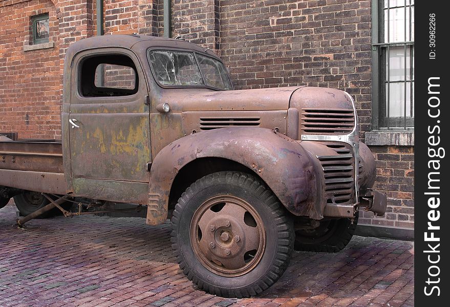 Front part of an old rusty truck with a broken windshield in a brick alleyway next to a brick wall. Front part of an old rusty truck with a broken windshield in a brick alleyway next to a brick wall.