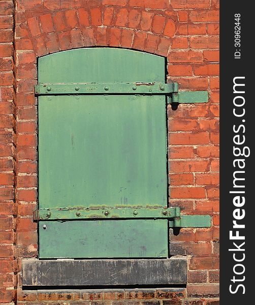 Old, worn, and weathered small closed green solid metal door in the brick wall of an old factory. Old, worn, and weathered small closed green solid metal door in the brick wall of an old factory