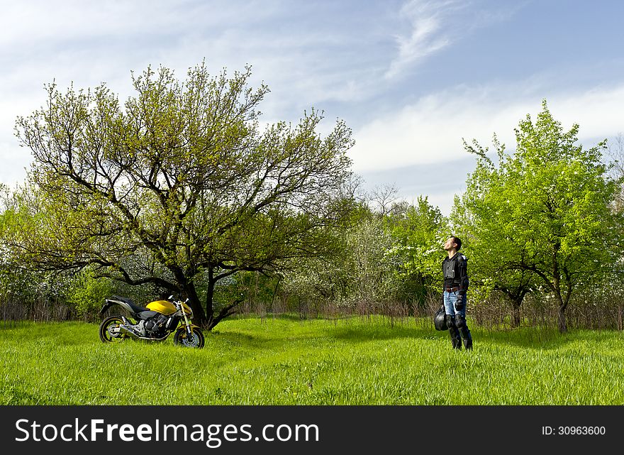 Biker with a sport motorbike resting against a nature calm landscape with a blue cloudy sky and breathes a scent of a spring fresh air. Biker with a sport motorbike resting against a nature calm landscape with a blue cloudy sky and breathes a scent of a spring fresh air.