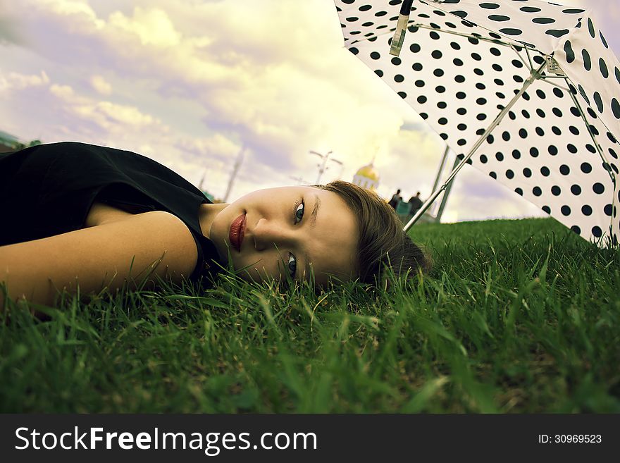 Beautiful girl lies on a green lawn with umbrella