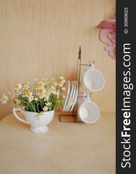 On a beige background white cup on a stand, and one with a bouquet of daisies. On a beige background white cup on a stand, and one with a bouquet of daisies