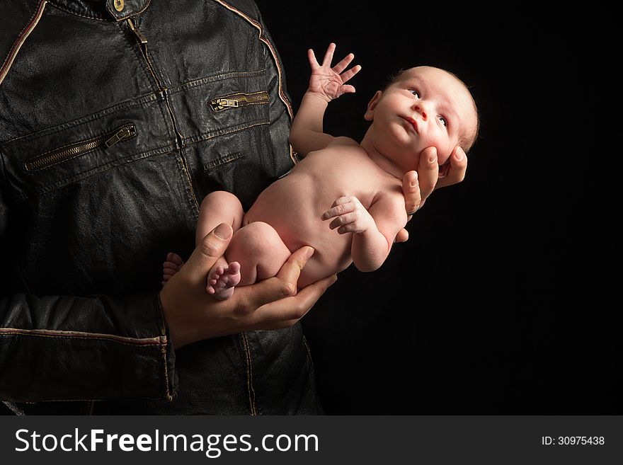 A father in a motorcyclist jacket holds his newborn son. A father in a motorcyclist jacket holds his newborn son