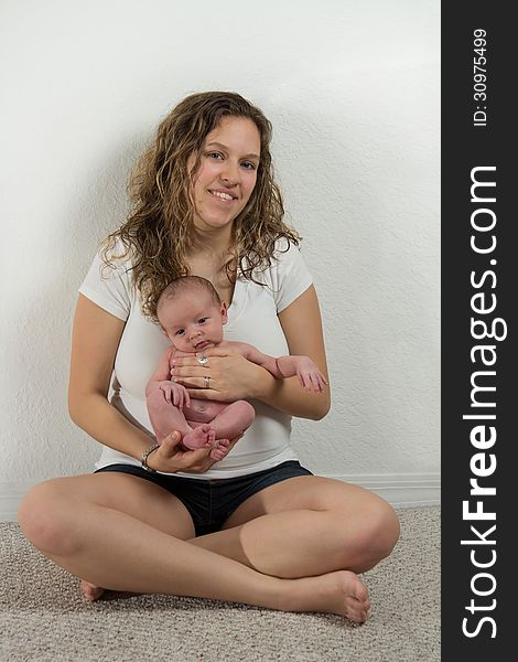 A mother holds her new baby next to white wall. A mother holds her new baby next to white wall