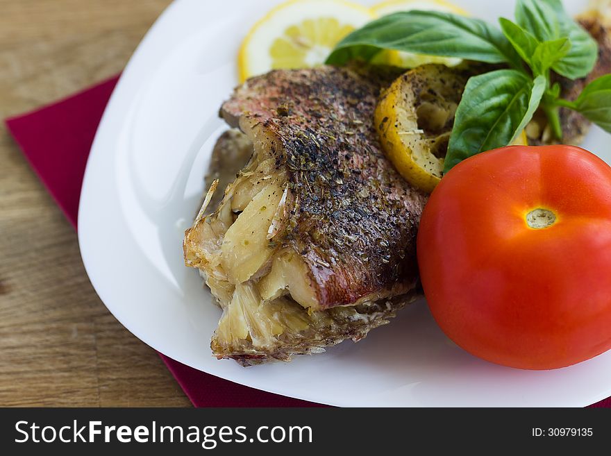 Baked grouper served with lemon and basil on white plate with tomato