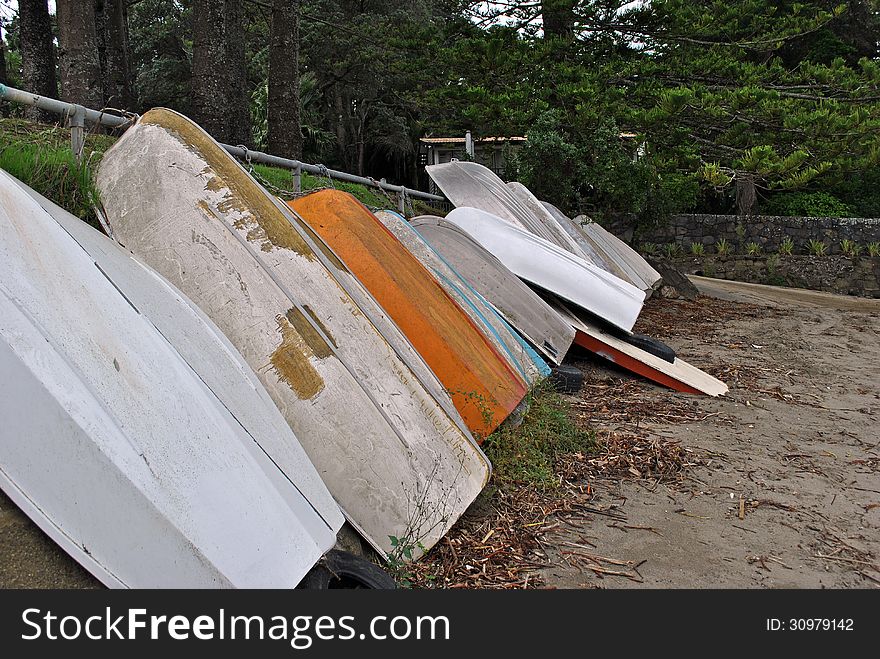 Row of assorted old and new row boats/dingys chained to a metal bar on the beach. Row of assorted old and new row boats/dingys chained to a metal bar on the beach