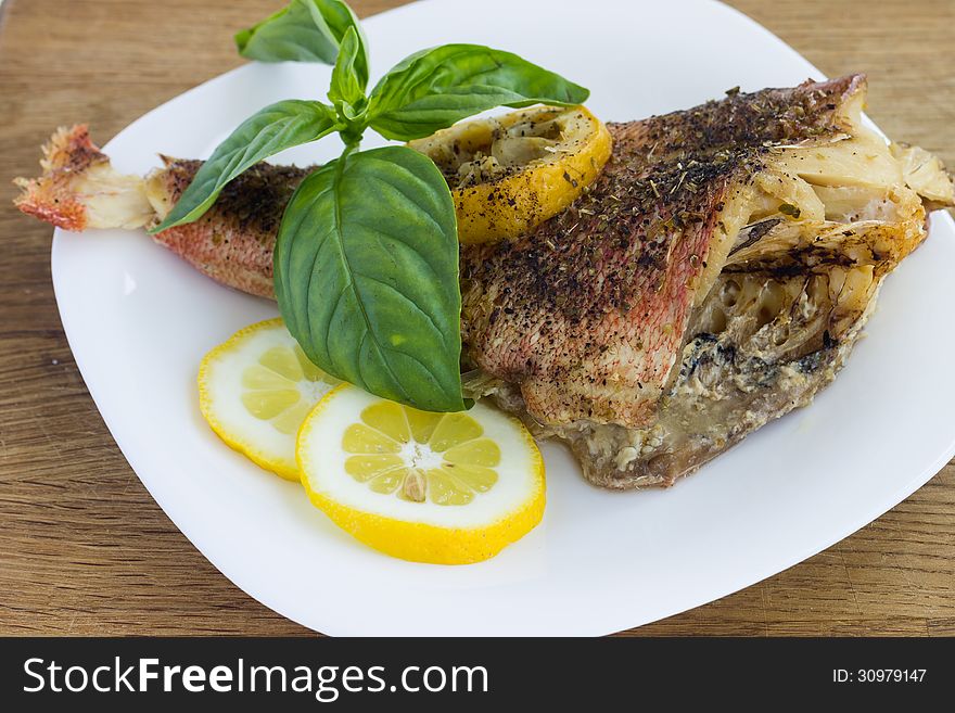 Baked grouper served with lemon and basil on white plate