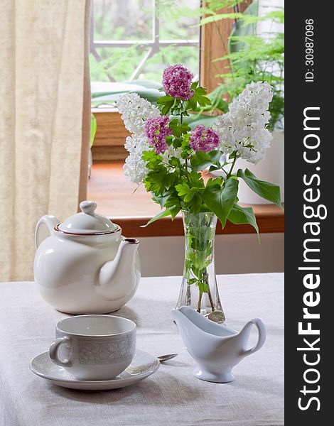 Teapot, teacup, milk jug and lilacs in a glass vase. Teapot, teacup, milk jug and lilacs in a glass vase