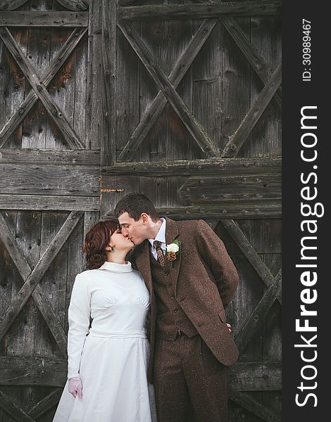 Wedding couple dressed in vintage dress and suit kissing each other with wooden door behind them. Wedding couple dressed in vintage dress and suit kissing each other with wooden door behind them.