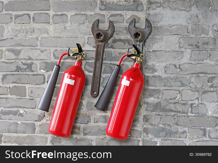 Fire extinguishers and spanners hanged on brick wall.
