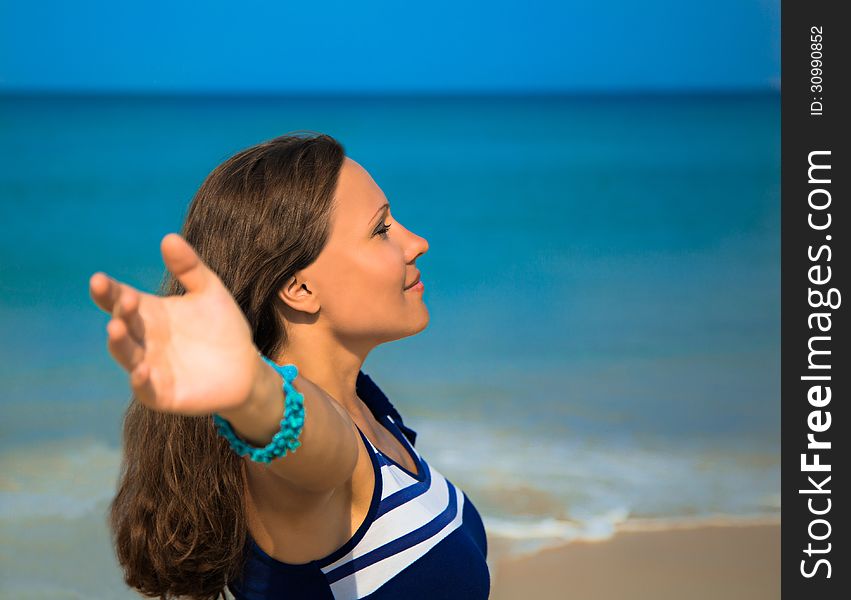 The young woman standing on a beach and looking afar with raised hands