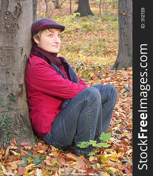 Model in vizored cap and muffler sitting by the tree. Model in vizored cap and muffler sitting by the tree