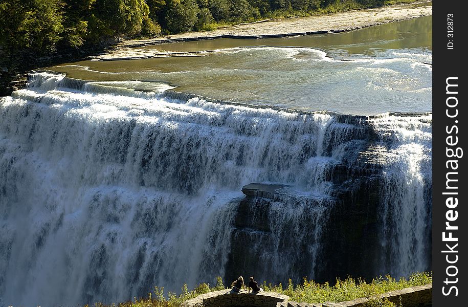 A couple sitting together viewing a waterfall - wide view with the river. A couple sitting together viewing a waterfall - wide view with the river