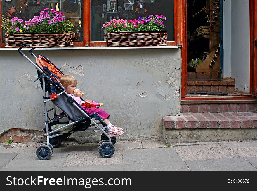 2-3 years old child sitting in the pram in front of the shop doors, eating ice cream and waiting for parent. 2-3 years old child sitting in the pram in front of the shop doors, eating ice cream and waiting for parent