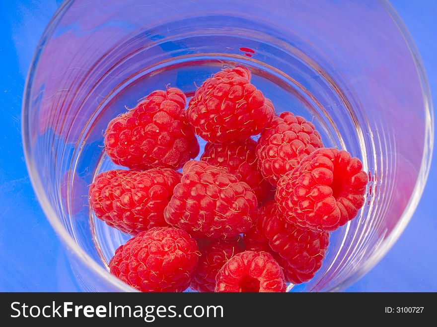 Red raspberry in  glass on  blue background