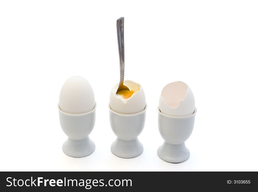 A whole egg, an egg with a spoon and an egg shell in eggcups on white background. A whole egg, an egg with a spoon and an egg shell in eggcups on white background.