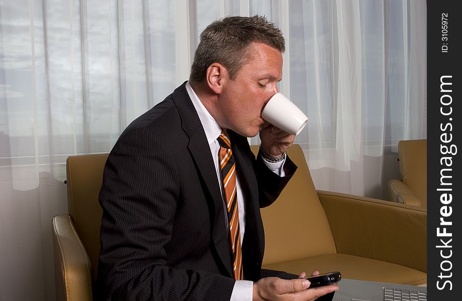 A man in shirt and tie reading a email and drinking coffee. A man in shirt and tie reading a email and drinking coffee