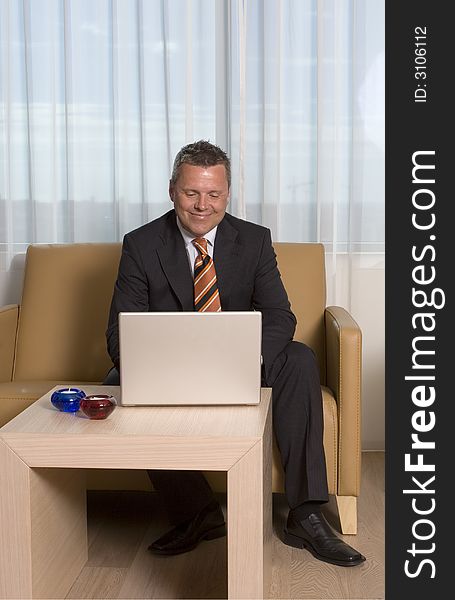 Businessman smiling working on his laptop sitting in sofa. Businessman smiling working on his laptop sitting in sofa