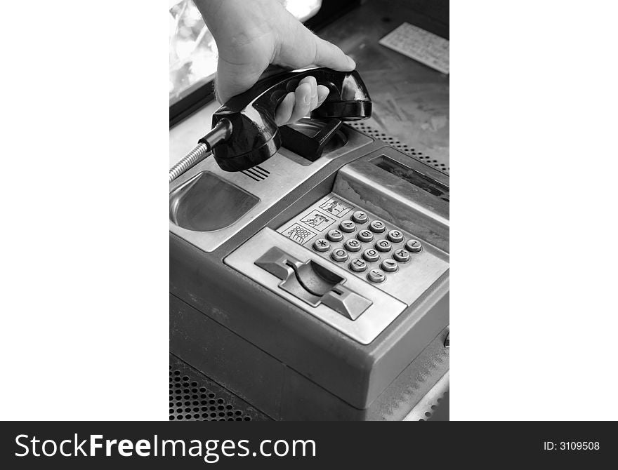 Black and white photo of public telephone close up with the receiver in hand