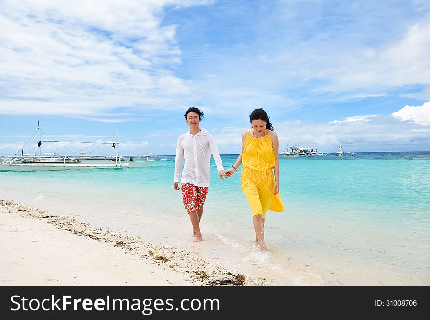 Happy young couple walks in shallow water on tropi
