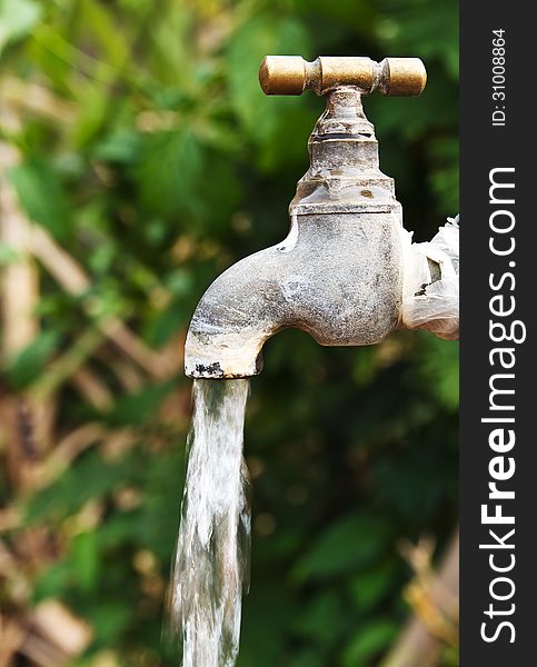 Old rusty tap leaking water in the garden