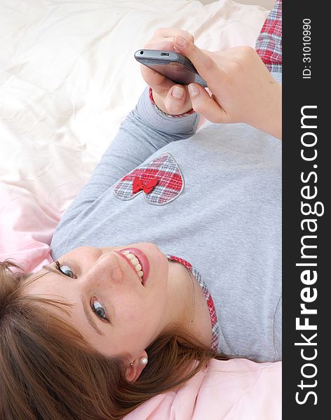 Young woman lying down on bed and sending cell phone text. Young woman lying down on bed and sending cell phone text.