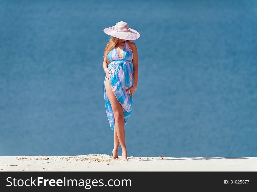 Young woman with blue water on the white sand in the pink hat. Young woman with blue water on the white sand in the pink hat