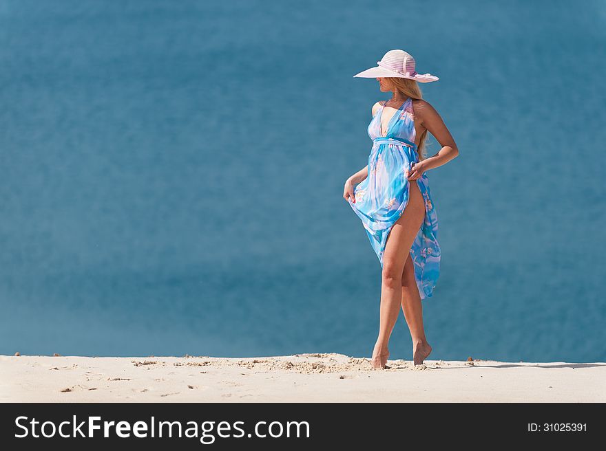 Young woman with blue water on the white sand in the pink hat. Young woman with blue water on the white sand in the pink hat