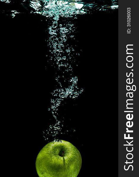 Green apple with splashing water on a black background. Green apple with splashing water on a black background