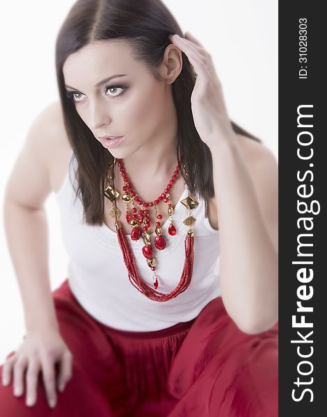 Portrait of young gorgeous woman wearing vivid necklace of red color beads. Dressed in red skirt and white t-shirt. Selective focus. Shot in studio. Over white background. Portrait of young gorgeous woman wearing vivid necklace of red color beads. Dressed in red skirt and white t-shirt. Selective focus. Shot in studio. Over white background.