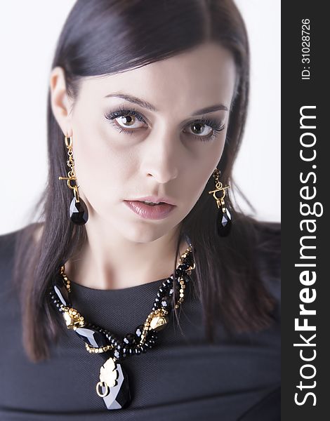 Close up portrait of young and beautiful glamour woman dressed in black cloth and wearing luxurious black stones jewelry- necklace and earrings, looking up straight to the camera. Shot in studio. Over white background. Close up portrait of young and beautiful glamour woman dressed in black cloth and wearing luxurious black stones jewelry- necklace and earrings, looking up straight to the camera. Shot in studio. Over white background.