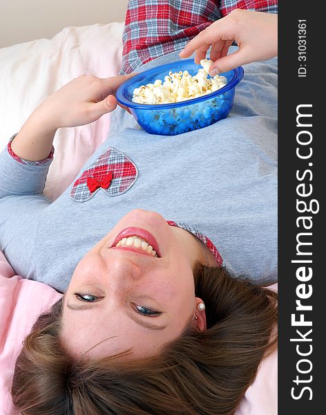 Beautiful young caucasian woman enjoying eating popcorn on her bed. Beautiful young caucasian woman enjoying eating popcorn on her bed.