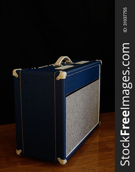 Vintage looking blue guitar amplifier against black backdrop on polished wooden floors. Vintage looking blue guitar amplifier against black backdrop on polished wooden floors