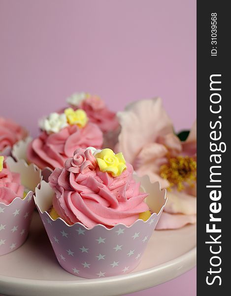 Beautiful pink decorated cupcakes on pink cake stand for birthday, wedding or female special event occasion,with pink flower. Vertical close up with bokeh. Beautiful pink decorated cupcakes on pink cake stand for birthday, wedding or female special event occasion,with pink flower. Vertical close up with bokeh.