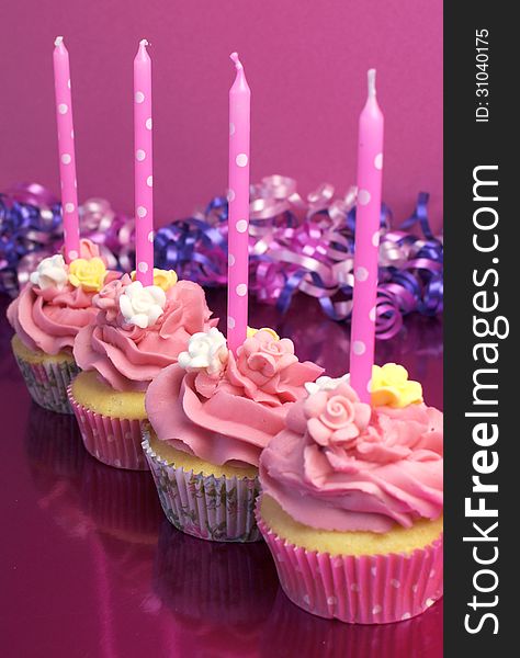 Pink brithday cupcakes with polka dot candles against a pink background. Vertical with shallow focus on second cupcake. Pink brithday cupcakes with polka dot candles against a pink background. Vertical with shallow focus on second cupcake.